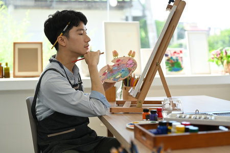 Concentrated man painting picture on canvas in art workshop. Leisure activity, creative hobby and...