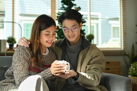 Loving young couple relaxing on comfortable couch, drinking hotchocolat and enjoying Christmas morning at home.の写真素材