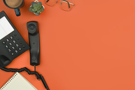 Above view of telephone, notepad, coffee up and eyeglasses on orange background. Flat lay, top view with copy space.の写真素材
