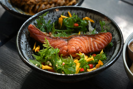 Close up view of fried salmon steak with edible wild flowers and vegetables on wooden table.