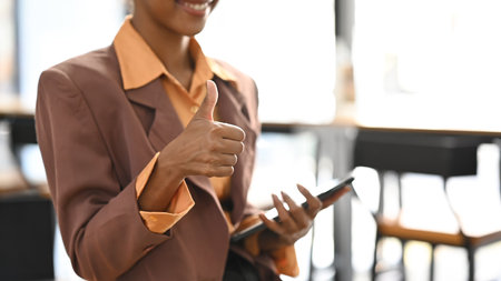 Cropped image go businesswoman in stylish suit holding tablet and showing thumbs up.の写真素材