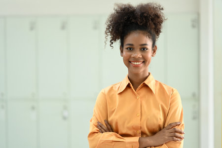 Portrait of American African female employee standing with crossed arms and smiling to camera.の写真素材