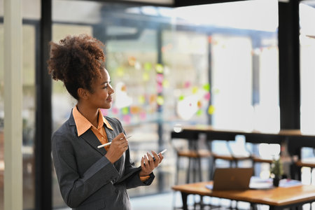 Photo of smiling African American female employee using digital tablet while standing in contemporary office.の写真素材