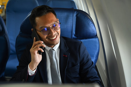 Successful businessman in suit talking on mobile phone while sitting comfortable seat in airplane cabin.の写真素材