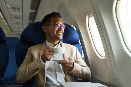 Positive businessman passenger drinking coffee from paper cup while sitting comfortable seat in airplane cabin.の写真素材