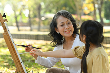 Positive mature grandmother and little granddaughter painting picture, enjoying leisure weekend hobby activity together outdoor.の写真素材