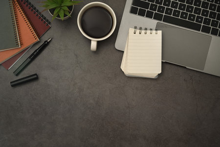 Top view of laptop computer, blank notepad, coffee cup and books on black slate texture background.の写真素材