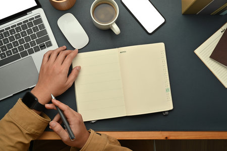 Creative male freelancer using laptop and making important notes, planning daily appointment on...