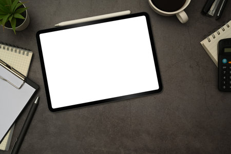 Flat lay digital tablet with white blank screen, cup of coffee and notepad on black slate texture background.の写真素材