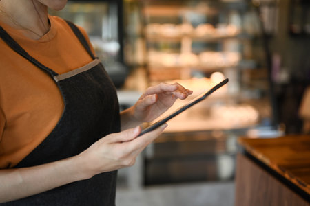 Cropped shot of female waitresses in apron using tablet and checking inventory in modern coffee shop.の写真素材