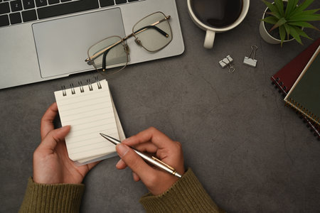 Above view of woman hand holding pen writing on empty notepad, working in creative workspace.の写真素材