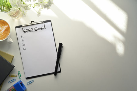 Clip board with 2023 goals list text, book and coffee cup on table. New year resolutions, goals, plan, action and checklist concept.の写真素材