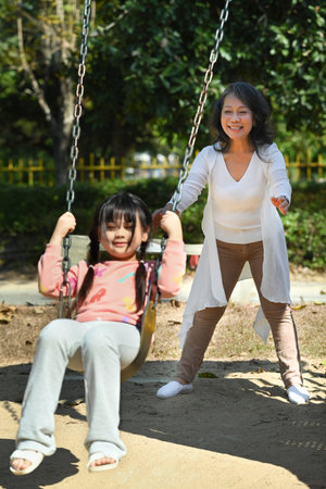 Joyful little girl having fun on swing with grandmother, spending weekend time together. Generational, family and love concept.の写真素材