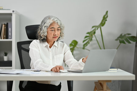 Focused middle age woman watching online webinar on laptop and using digital tablet during remote working from home.の写真素材