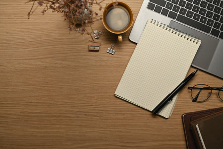 Empty notepad, eyeglasses, pen and laptop computer on wooden working desk. Top view with copy space.の写真素材