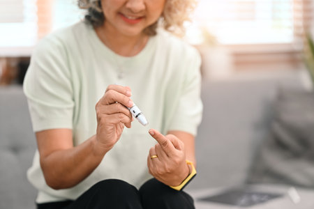 Cropped shot of diabetic mature lady taking blood sample with lancet pen. Diabetes and elderly healthcare concept.の写真素材