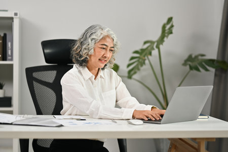 Successful middle aged businesswoman using laptop computer in modern office.の写真素材