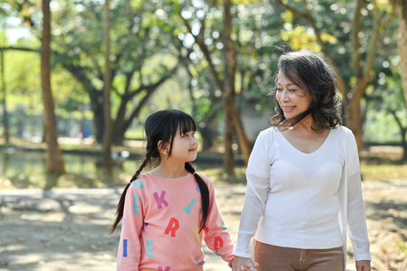 Adorable little child and elderly grandmother walking in the park, spending time outdoor together. Family and love concept.の写真素材