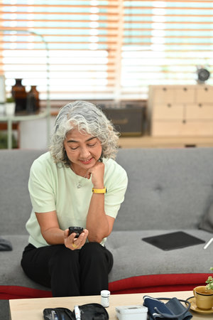 Senior woman sitting on couch and checking blood glucose levels with a glucose meter. Diabetes and health care concept.の写真素材