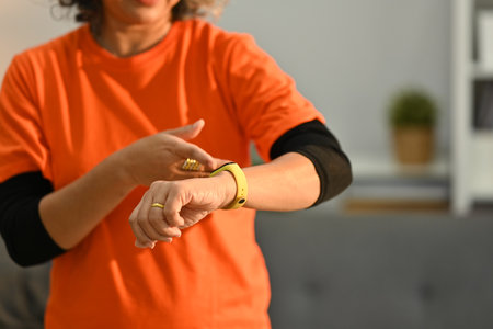 Cropped shot of middle age woman checking fitness results or heart rate on smartwatch during workout at home.の写真素材