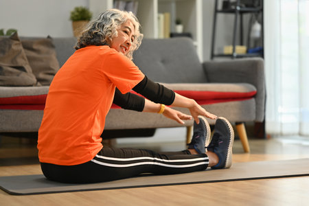 Middle aged woman in sport clothes stretching her legs before working out at home. Healthy lifestyle...