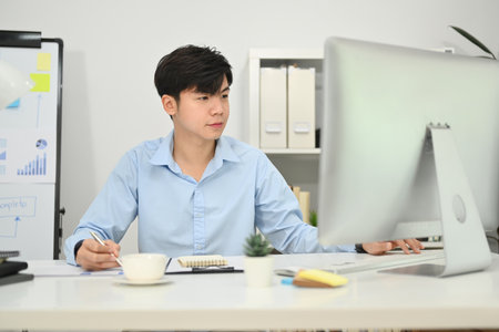 Asian business man manager looking at computer monitor watching online webinar training at his workplace.の写真素材