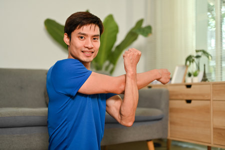 Smiling sporty asian stretching arms before workout out at home. Healthy lifestyle and fitness concept.の写真素材