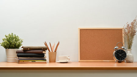Simple workplace with blank cock board alarm clock, books and potted plant on wooden table.の写真素材