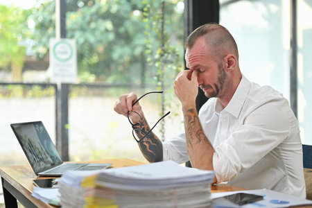 Overworked caucasian man worker holding glasses and rubbing nose suffering from chronic dry eye syndrome bridge.の写真素材