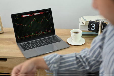 Cropped shot of young male trader sitting in his office in front of laptop computer screens with...