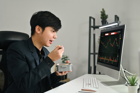 Young businessman or trader sitting at his office in front of computer screen and enjoying lunch break.の写真素材