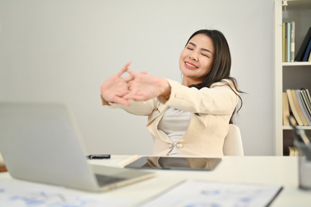 Happy asian female worker stretching arms, relaxing on comfortable office chair in modern office.の写真素材