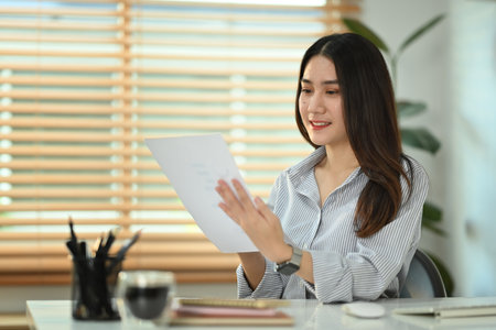 Smiling young female economist preparing report, analyzing work results at workplace.の写真素材