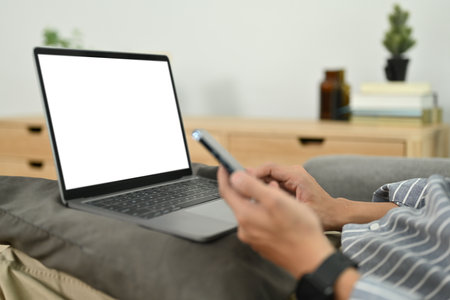 Cropped image of man sitting on couch with laptop and chatting on mobile phone. People. technology and communication concept.の写真素材