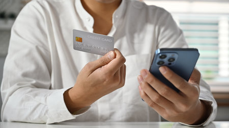 Cropped image of man holding using mobile phone and credit cad for online banking transaction, ordering in internet.の写真素材
