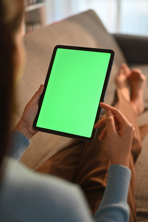 Close up view of casual young woman using digital tablet on couch at home. Green screen for montage your graphic display.の写真素材