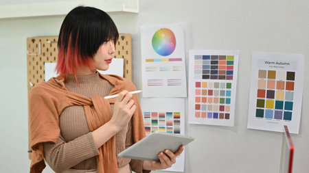 Young asian woman designer illustrator standing in modern design studio and using digital tablet.の写真素材