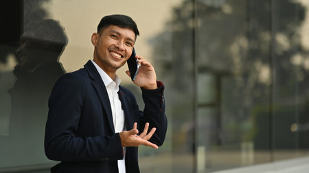 Handsome successful businessman standing near modern office building in city and talking on mobile phone.の写真素材