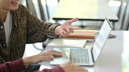 Cropped shot of university students sitting at campus library desk, doing group project and using laptop.の写真素材