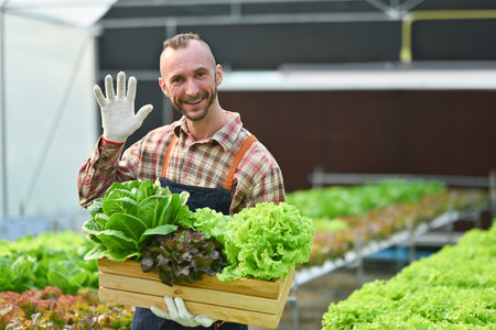 Successful small business owner holding a wooden crate with fresh organic vegetables standing in greenhouse.の写真素材