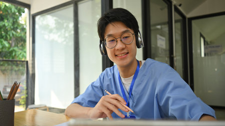 Head shot young doctor wearing blue scrubs giving consultation patient online. Therapist online, telemedicine concept.の写真素材