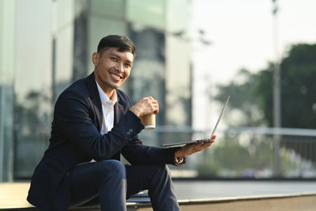 Successful start up businessman using laptop on stairs in front of business center. Modern lifestyle, business, technology concept.の写真素材