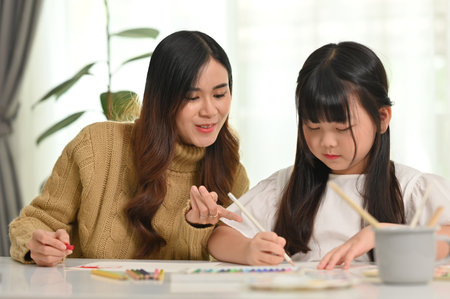 Happy asian mother and little daughter coloring a picture, doing a hobby or education project together at home.の写真素材