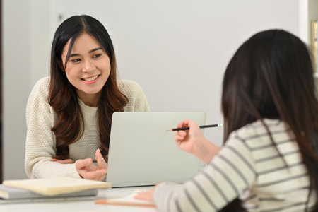 Smiling young mother and little daughter doing homework, learning at home. Homeschooling concept.の写真素材