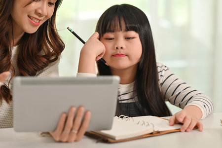 Bored little student girl doing homework with mother at home. Homeschooling and education concept.の写真素材