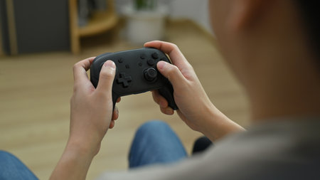 View over shoulder of young man holding wireless controller playing video game. Entertainment,...