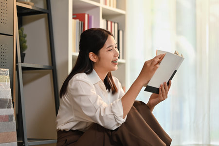 Beautiful young woman sitting floor in living room and reading a book, spending leisure weekend time at home.の写真素材