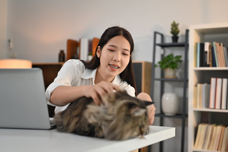 Asian woman playing her cat on theAsian woman playing her cat on the table in modern home office. table in modern home office. High quality photoの写真素材