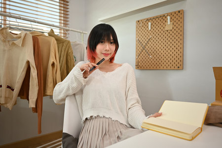 Young female fashion designer standing near clothing rack, working on new womenswear collection in modern studio.の写真素材