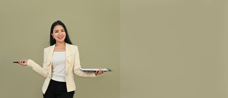 Confident asian businesswoman in stylish suit holding clipboard standing isolated over gray background. Copy space for your text.の写真素材